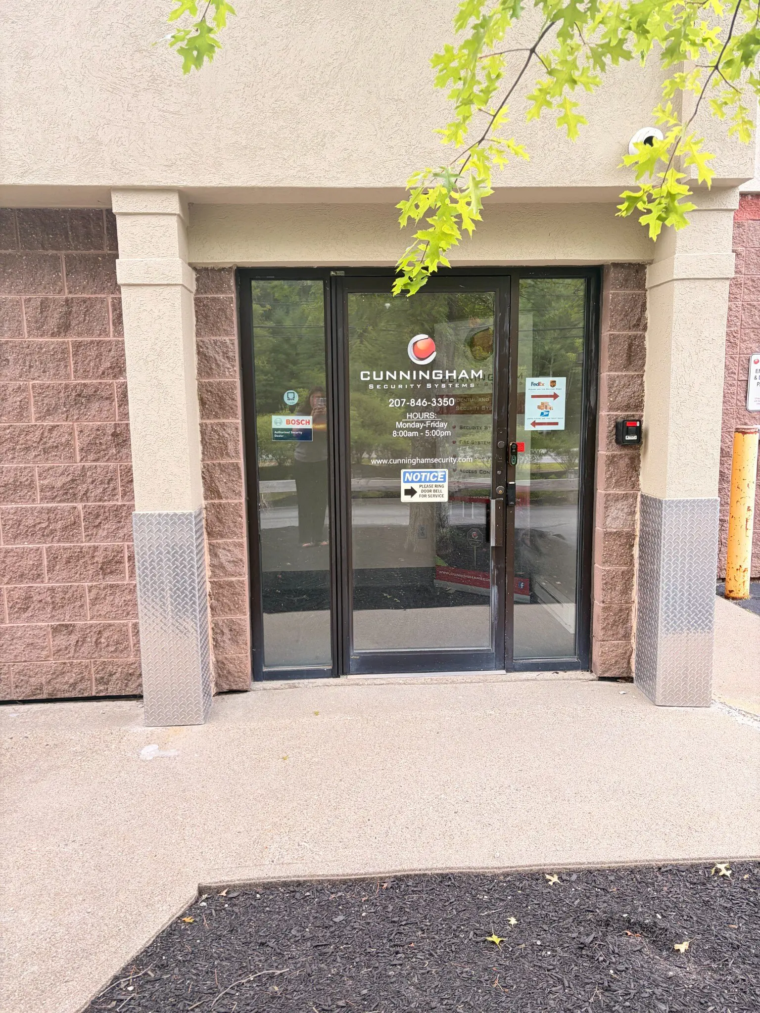 Cunningham Security Systems glass entrance door with posted hours, phone number and a notice asking visitors to ring the doorbell for service