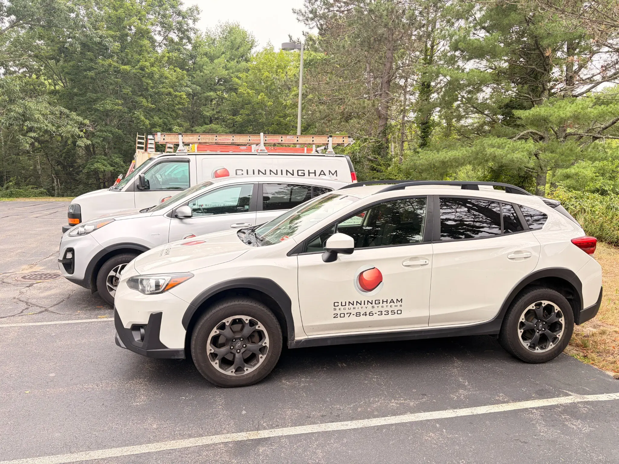 A marked Cunningham Security Systems Subaru and a ladder-equipped service van parked outside the Falmouth office