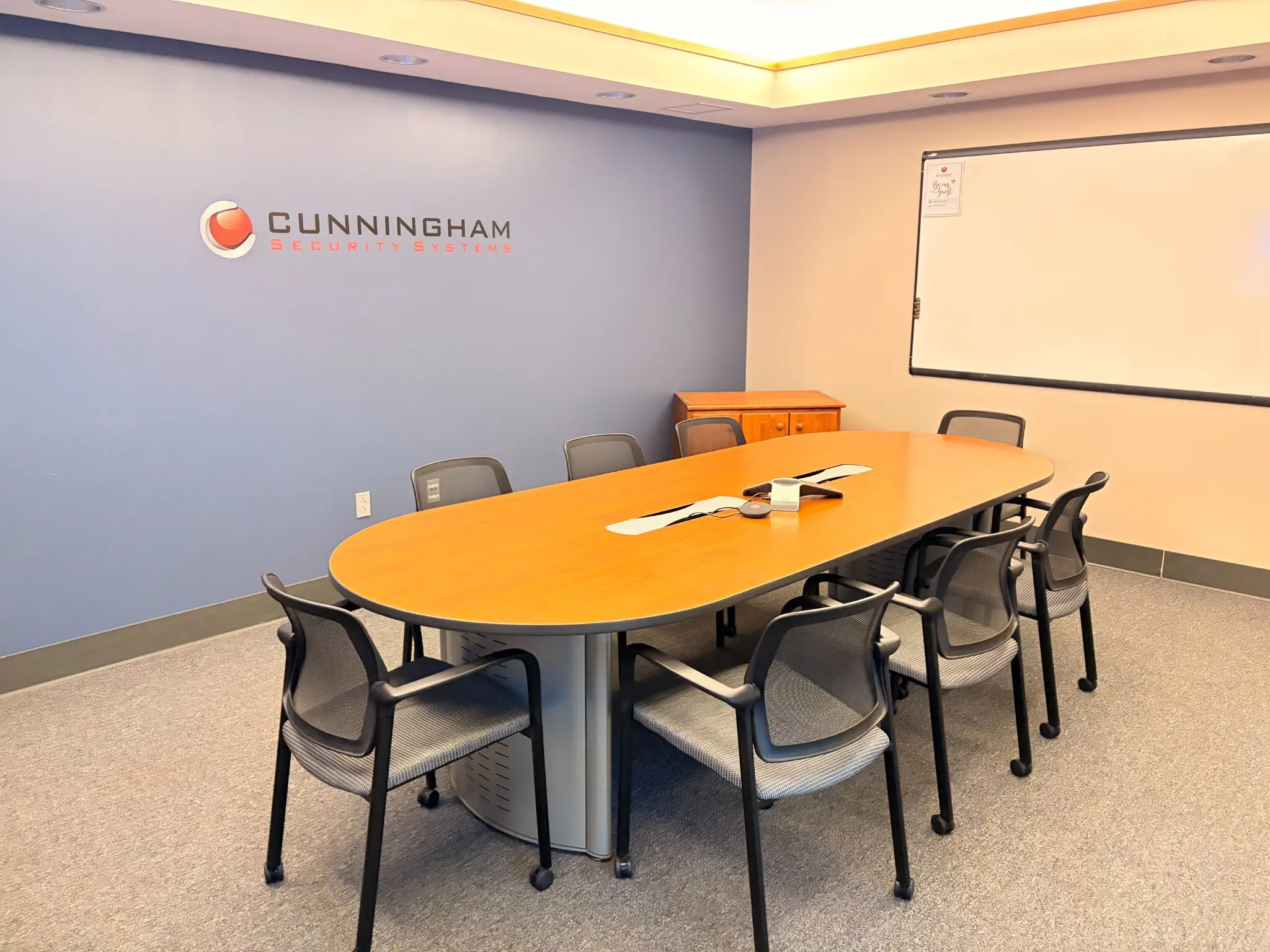 Conference room at the Falmouth office with the Cunningham Security Systems logo on the wall, an oval table and seating for eight